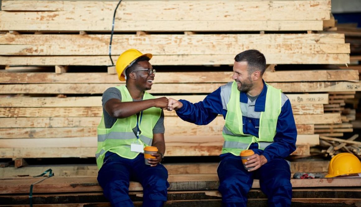 Happy warehouse workers greeting with fists while working at wood compartment.