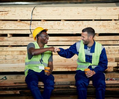 Happy warehouse workers greeting with fists while working at wood compartment.